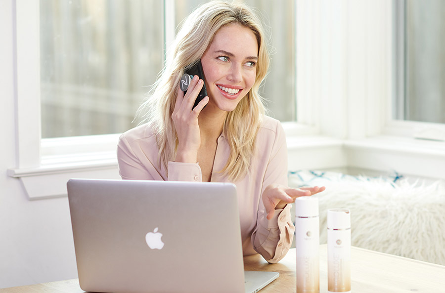 Neora Brand Partner in their home office connecting with customers while using a phone with a Neora pop socket on it. 